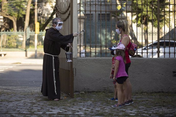 Un sacerdote esparce agua bendita sobre dos feligresas en Río de Janeiro.
