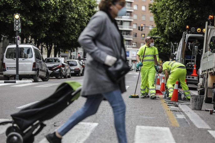 Una mujer cruza un paso de cebra junto al que varios operarios están  trabajando en el inicio de la remodelación de la calzada