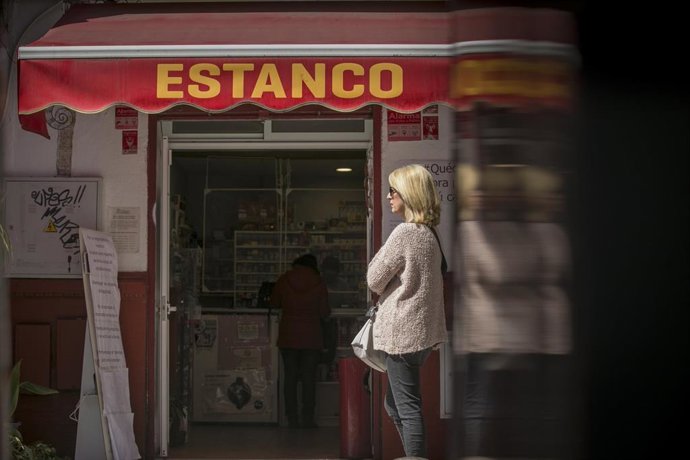 Una mujer guarda cola en un estanco, abierto por ser esencial, durante la limitación total de movimientos salvo de los trabajadores de actividades esenciales, medida adoptada por el Gobierno como prevención del coronavirus durante el estado de alarma. E