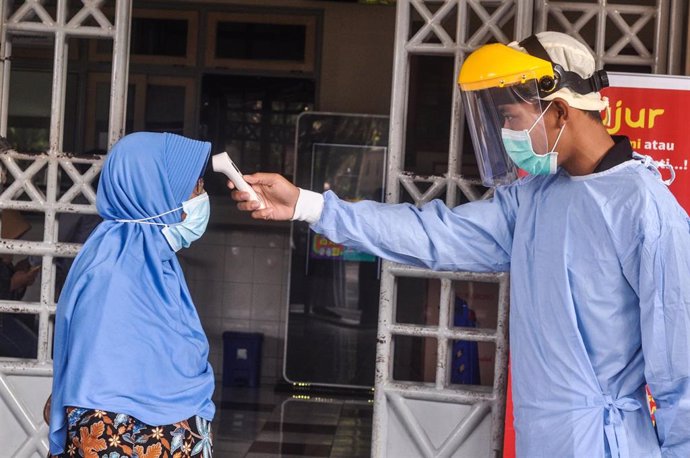 Un trabajador sanitario toma la temperatura a una mujer en Indonesia. 