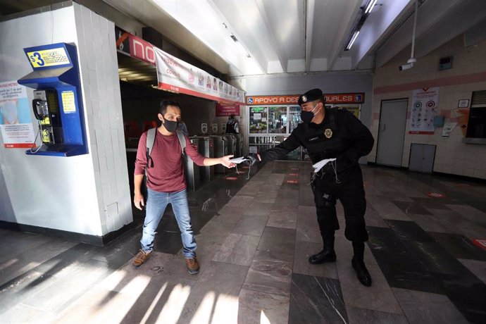 Un oficial de Policía entrega una mascarilla a un pasajero del metro en Ciudad de México.