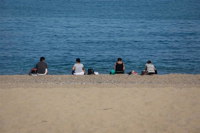 Varias personas sentadas en la playa de Barcelona respetan la distancia de seguridad por el coronavirus