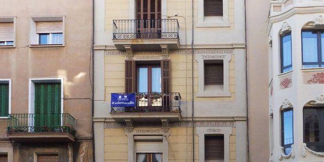 Un balcón de la ciudad de Barcelona con una bandera de la campaña 'Casa nostra, casa vostra' que reivindica el derecho al asilo de los migrantes procedentes de zonas en conflicto