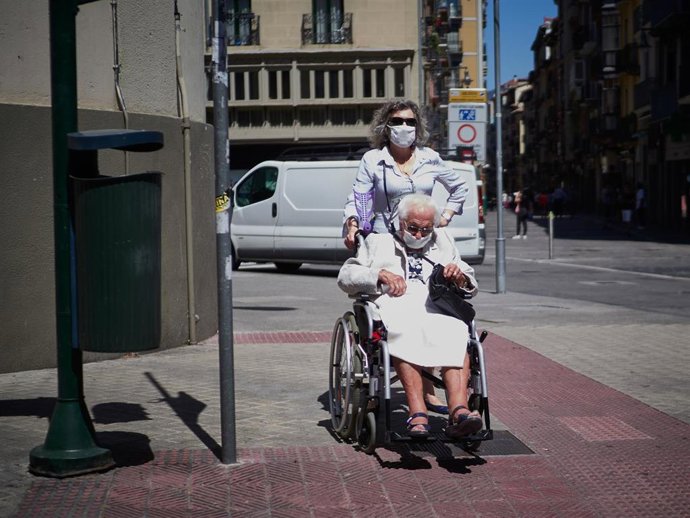 Una mujer pasea a una persona mayor, ambas protegidas con mascarilla, por las calles de Pamplona