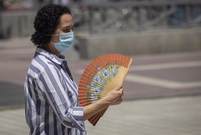 Una mujer con mascarilla se abanica mientras camina por Sevilla en un día de mayo con altas temperaturas