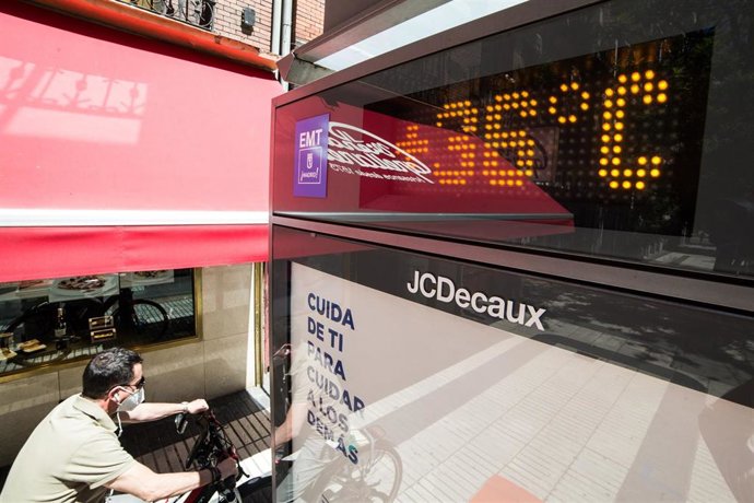 Un hombre pasa en bicicleta junto a un termómetro