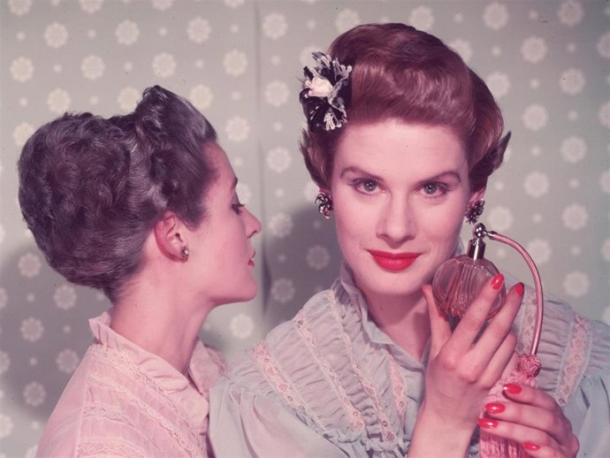 A woman with bright red nail varnish sprays herself with perfume using an atomiser.