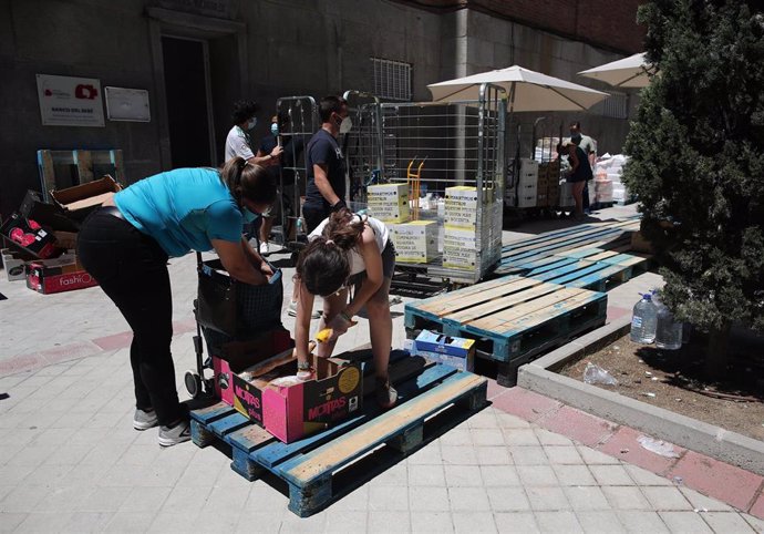 Una mujer recoge productos que le entrega una voluntaria a las puertas de la Parroquia Santa María Micaela. En Madrid (España), a 29 de mayo de 2020.
