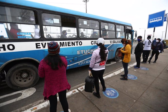 Un grupo de personas mantienen las distancias sociales mientras esperan en una parada de autobús de Lima, Perú.