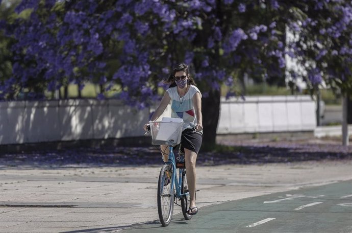 Una mujer con mascarilla y ropa de verano circula en bicicleta por el Puente del Alamillo. En Sevilla (Andalucía, España), a 21 de mayo de 2020.