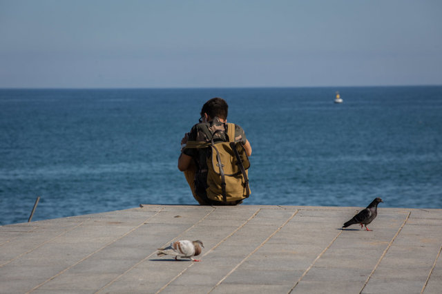 Un joven sentado en el Paseo Marítimo de la Playa de la Barceloneta durante el día 66 del estado de alarma.