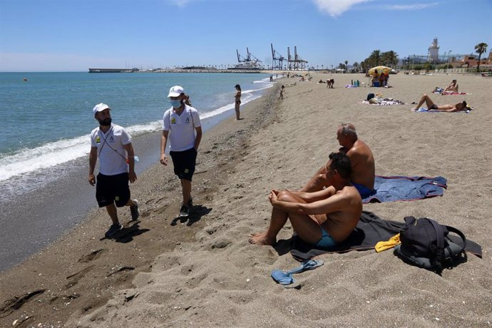 Una pareja de Vigilantes de la playa de Andalucía asesoran a bañistas sobre las medidas preventivas sobre el COVID-19 en la playa de La Malagueta. Málaga a 16 de junio del 2020