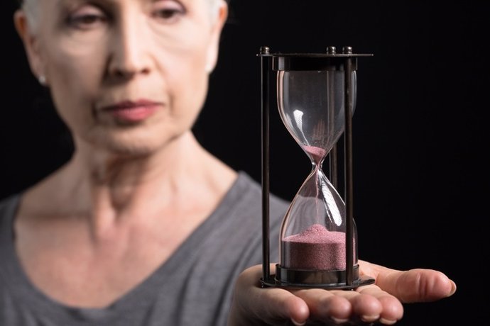 Senior woman holding sand clock isolated on black