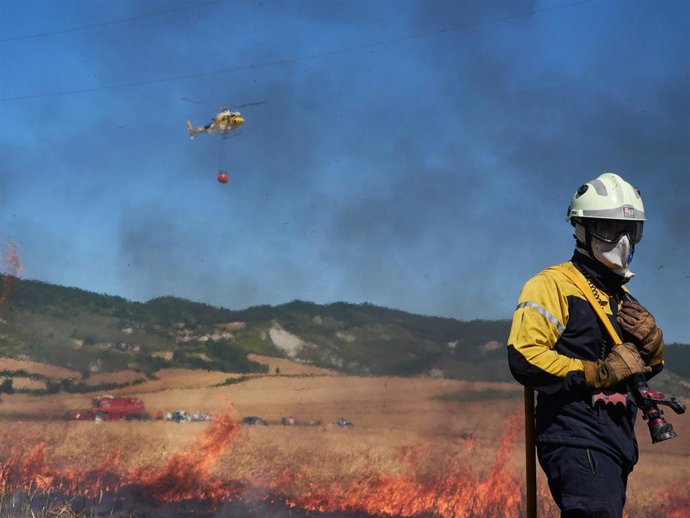 Un bombero y un helicóptero de la Brigada Helitransportada del Gobierno de Navarra realizan labores de extinción de un incendio forestal producido en una zona de campo de cereal, sin afectar a zonas urbanas, cerca de la localidad navarra de Sarriguren, 