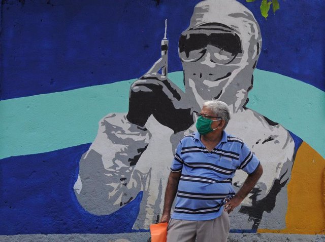 Un hombre con mascarilla ante un mural de un trabajador médico en Bombay