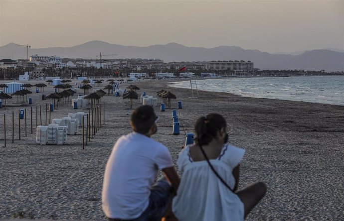 Dos jóvenes sentados contemplan la playa de la Malvarrosa durante la noche de San Juan en Valencia