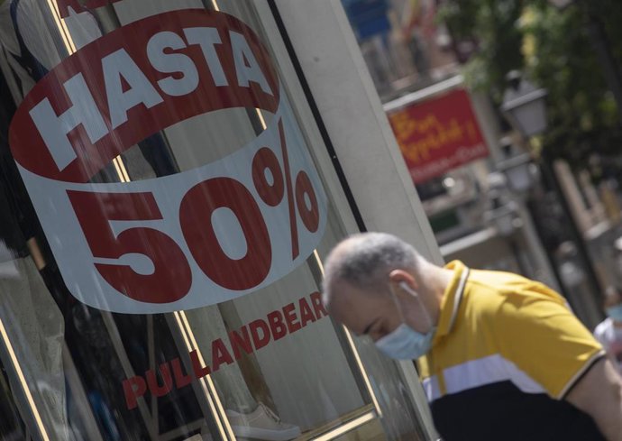 Una persona pasa al lado de un escaparate de una tienda de la capital con carteles de descuentos durante el segundo día de rebajas, en Madrid (España), a 26 de junio de 2020.