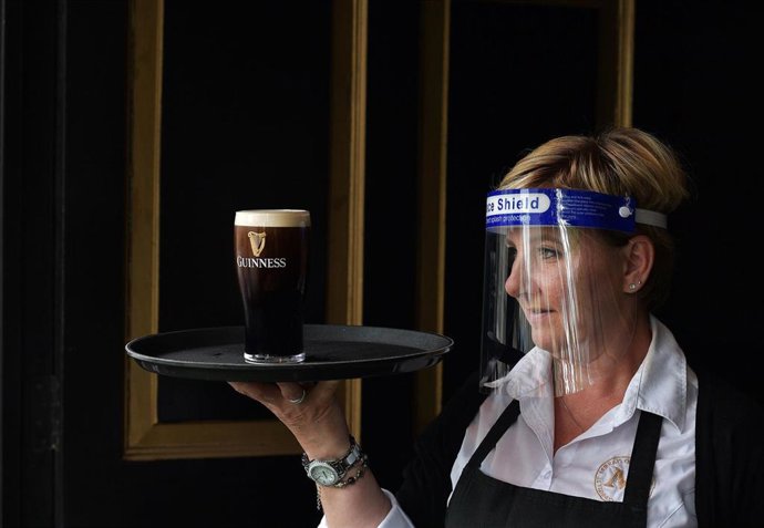 Camarera con protección frente al coronavirus con una bandeja con una pinta de cerveza negra en un pub de Dublín