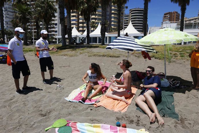 Una pareja de Vigilantes de la playa de Andalucía asesoran a bañistas sobre las medidas preventivas sobre el COVID-19 en la playa de La Malagueta. Málaga a 16 de junio del 2020