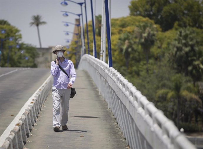 Un hombre con un gorro camina por la pasarela de la Cartuja durante la alerta naranja por altas temperaturas. En Sevilla (Andalucía, España), a 23 de junio de 2020.