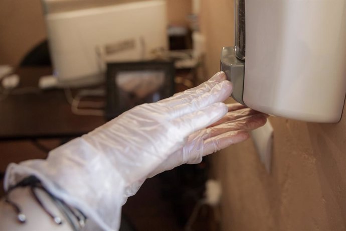 Un trabajador protegido con mascarilla coloca gel desinfectante en un dispensador para clientes 