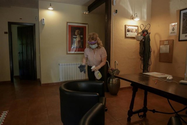 Una trabajadora protegida con mascarilla y mampara desinfecta dentro de las instalaciones de una casa rural