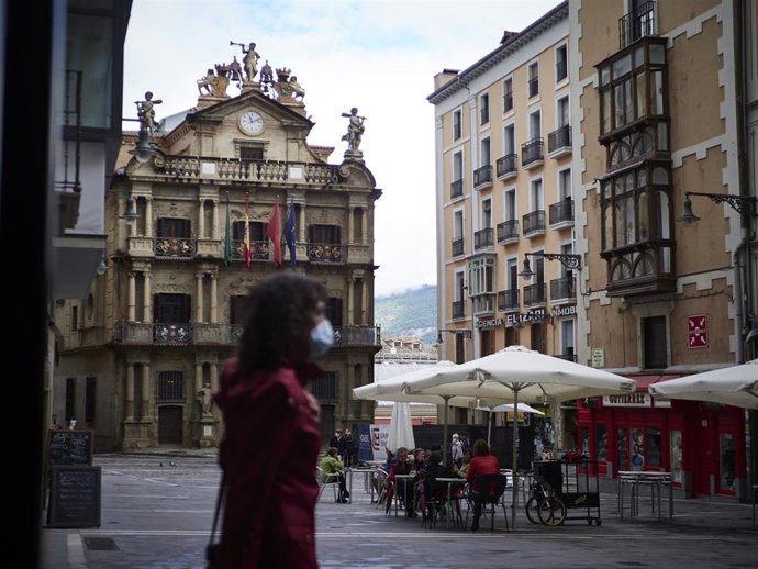Una mujer con mascarilla pasa al lado de una terraza abierta de Navarra donde los empleados utilizan un metro para asegurarse de que las medidas de distanciamiento son las correctas entre los potenciales clientes de la terraza de un bar en el centro de 