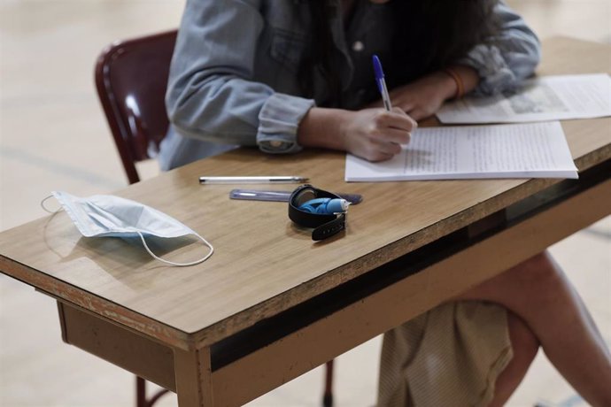 Un alumno de bachillerato del Colegio Virgen de Europa de Boadilla del Monte (Madrid) deja su mascarilla en el pupitre para enfrentarse a los primeros exámenes presenciales tras el parón por el coronavirus en el polideportivo del centro