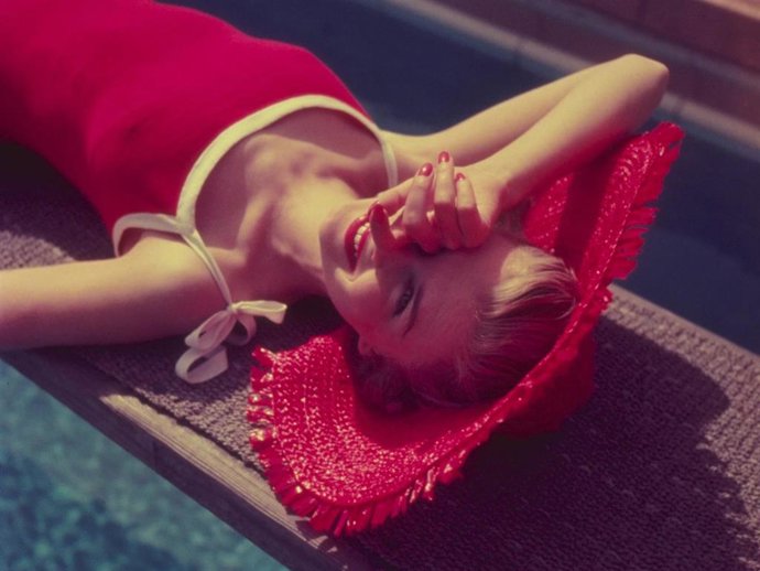 A woman in a red straw hat sunbathing on a diving board.