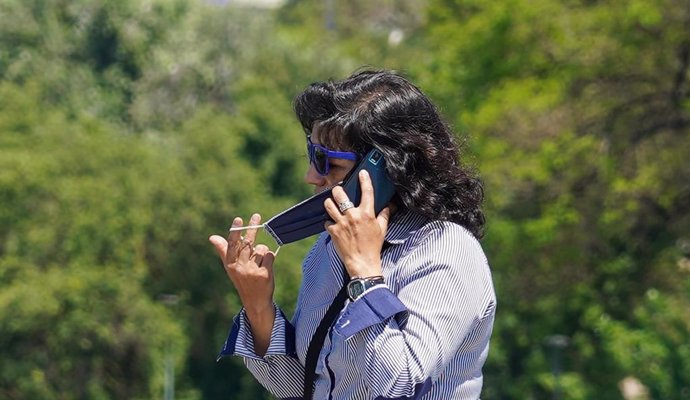 Una mujer se quita la mascarilla para hablar por teléfono mientras pasea por el puente de triana  en el  primer día del uso obligatorio de mascarillas por el Covid-19. Sevilla a 21 de mayo del 2020