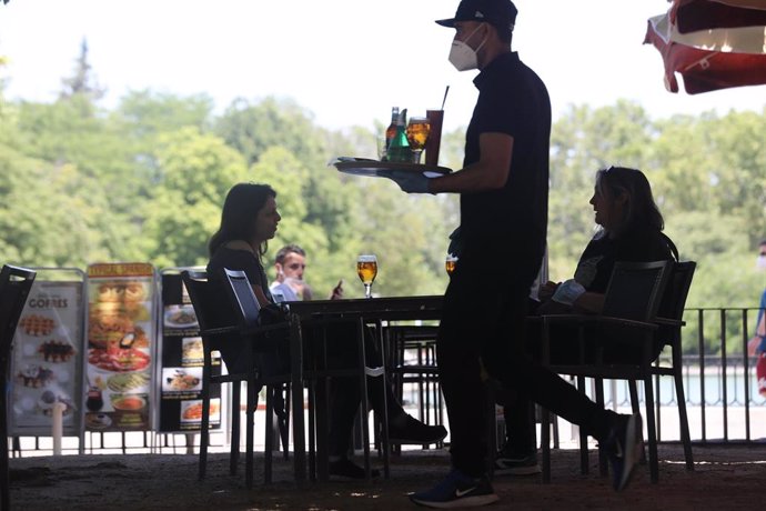 Un camarero protegido con mascarilla atiende a una mesa de una de las terrazas abiertas en el Parque de El Retiro