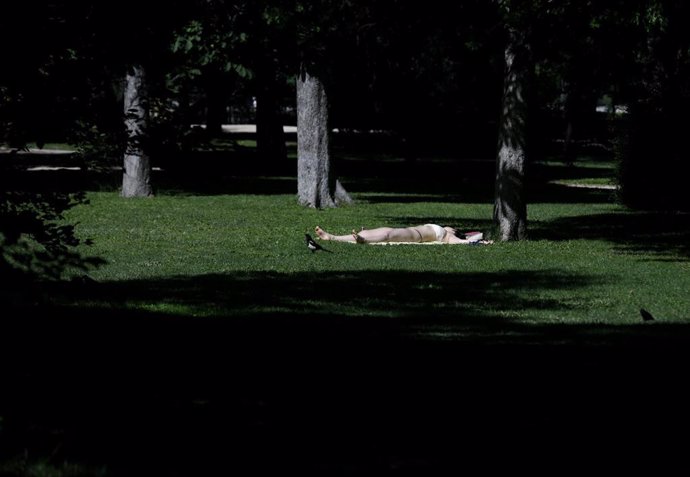 Una joven toma el sol en el césped en el Parque del Retiro en Madrid (España), a 29 de junio de 2020. El calor pone desde este lunes en aviso a una quincena de provincias de Andalucía, Castilla y León, Castilla-La Mancha, Extremadura y Madrid, por tempe
