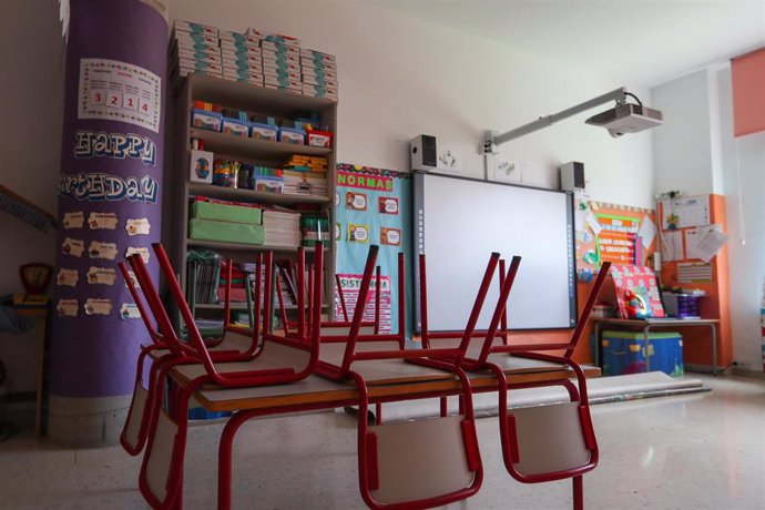 Mesas y sillas recogidas en un aula escolar.