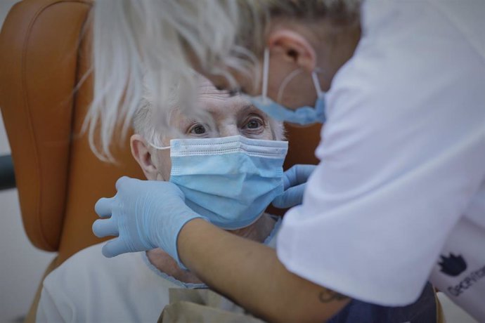 Una trabajadora le coloca una mascarilla a una residente.