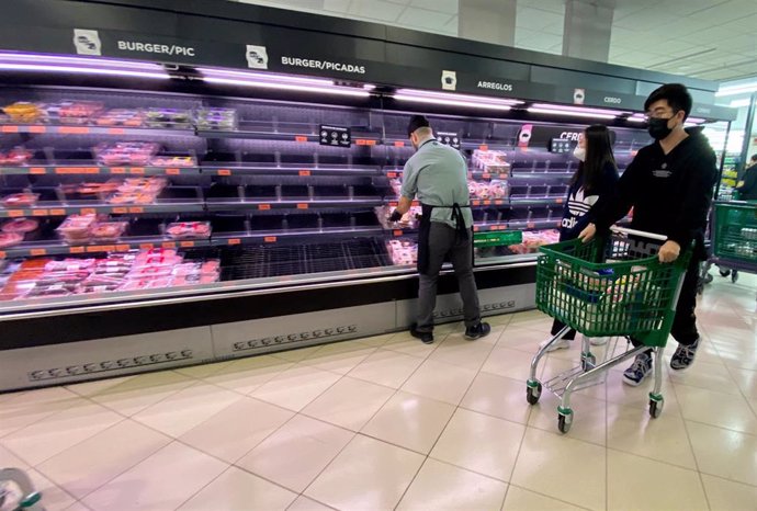 Una pareja con rasgos asiáticos y protegidos con mascarilla realizan la compra en un supermercado