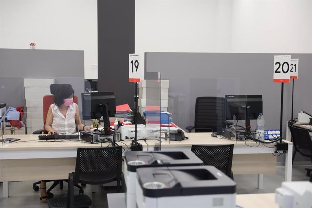 Una trabajadora de la Oficina del Empleador protegida con mascarilla y con una pantalla separadora en su mesa 