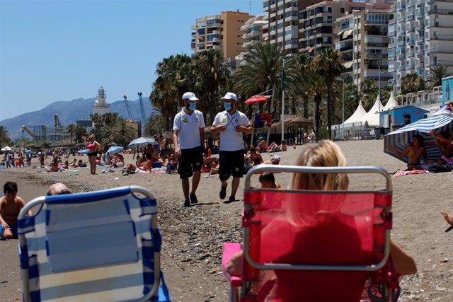 Una pareja de Vigilantes de la playa de Andalucía asesoran a bañistas sobre las medidas preventivas sobre el COVID-19 en la playa de La Malagueta. Málaga a 16 de junio del 2020