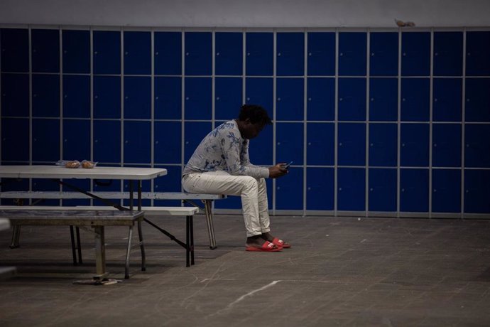 Un hombre sentado en un banco consulta su móvil en el interior de las instalaciones del albergue de Fira Barcelona, habilitado por la crisis de la pandemia del coronavirus para 225 personas sin techo desde el pasado 25 de marzo, a 28 de mayo de 2020.