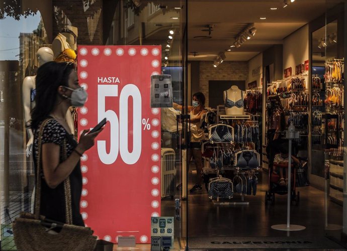 Una mujer protegida con mascarilla pasa al lado del escaparate de una tienda donde se observan carteles indicativos de rebajas en Valencia, Comunidad Valenciana (España) a 3 de julio de 2020. El 61% de los consumidores gastará 129 euros de media en las 