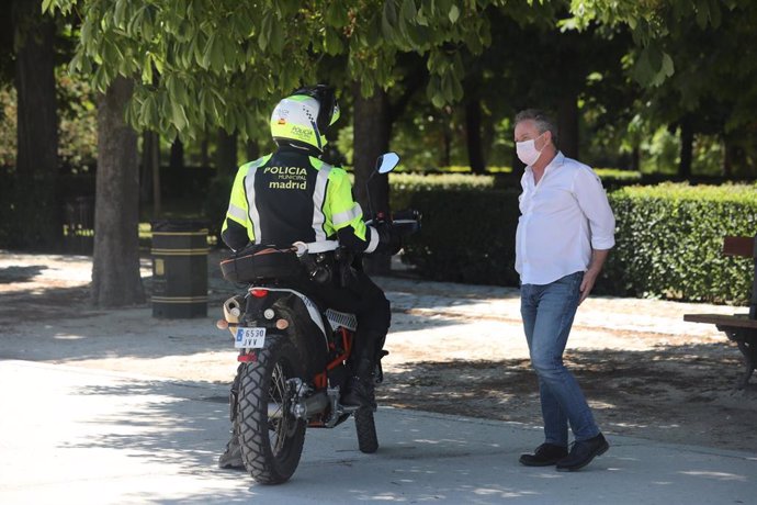 Un policía municipal habla con un transeúnte que camina por el Parque de El Retiro