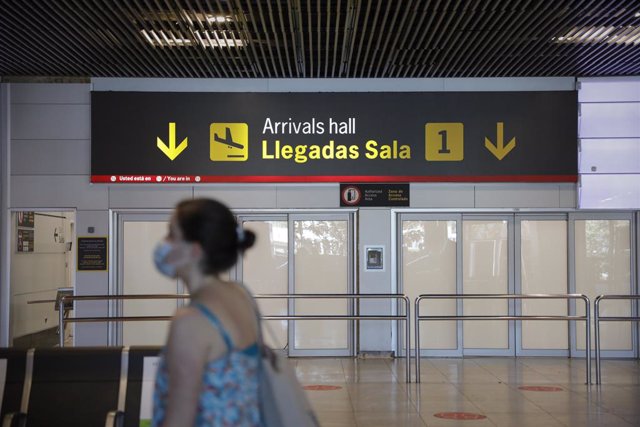 Una persona con mascarilla pasa junto a la entrada de la sala de llegadas 1 de la Terminal 1 del Aeropuerto de Barajas, en Madrid (España)