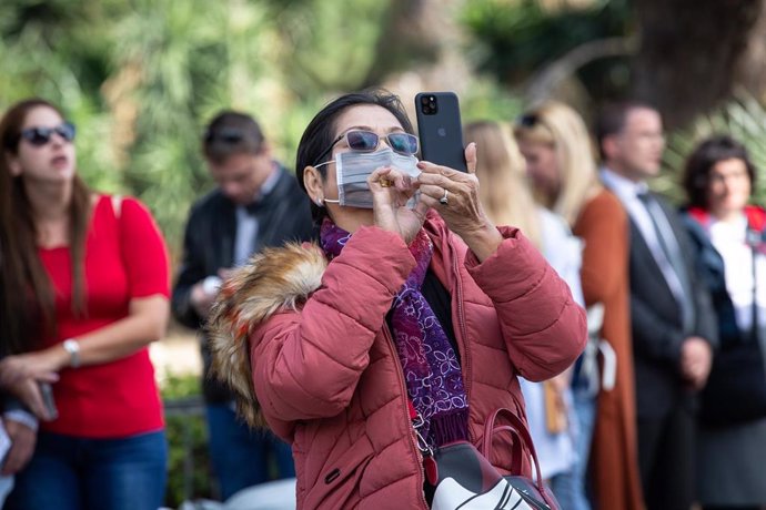 Una turista con mascarilla fotografía un monumento con su teléfono móvil.