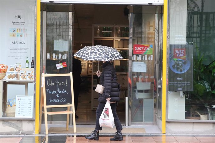 Una mujer pasea con un paraguas frente a un establecimiento abierto en la capital en un día de lluvia y bajada de temperaturas en toda España