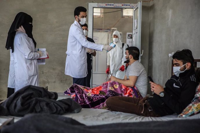 Un médico toma la temperatura de dos refugiados sirios que permanecen en cuarentena dentro de unas instalaciones habilitadas cerca de la frontera con Turquía.