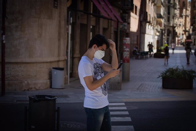 Un joven con mascarilla camina mirando el móvil.