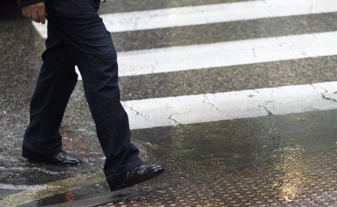 Un hombre mayor pisa un charco formado por las lluvias que han caído en Madrid al cruzar un paso de peatones.