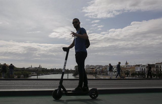 Un joven atraviesa el Puente de Triana de Sevilla con un patinete eléctrico