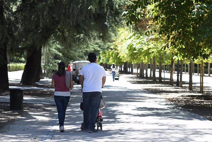 Una pareja pasea con su bebé en un carrito por un parque de Madrid.