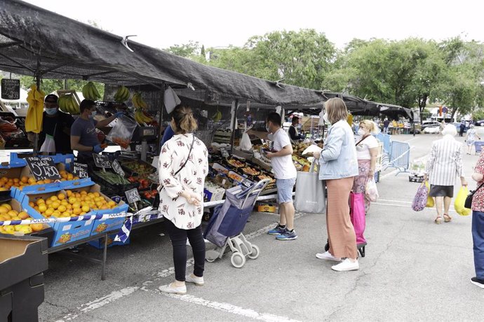 Varias personas hacen cola frente a un puesto de fruta en el mercadillo