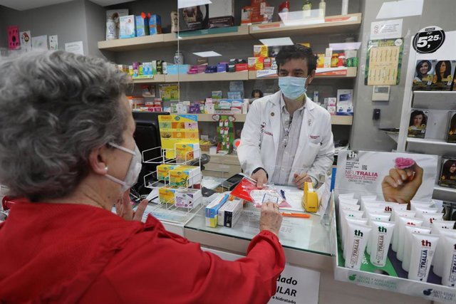 Un farmaceútico entrega una mascarilla a una usuaria. En Madrid (España), a 11 de mayo de 2020.